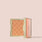 Jouer Brightening Powder open compact in warm orange with embossed logo pattern on a beige background.