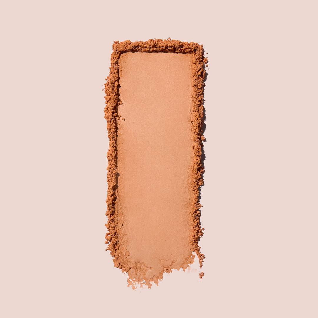 Jouer Brightening Powder swatch in warm peach-orange showing the rich, buttery texture on a beige background.