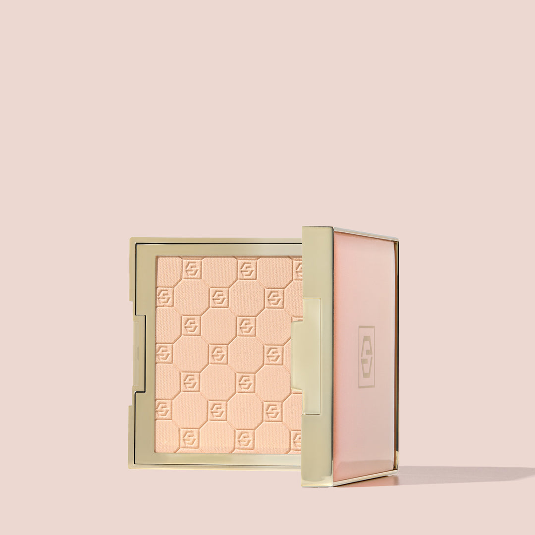 Jouer Brightening Powder open compact in light peach with embossed logo pattern on a beige background.