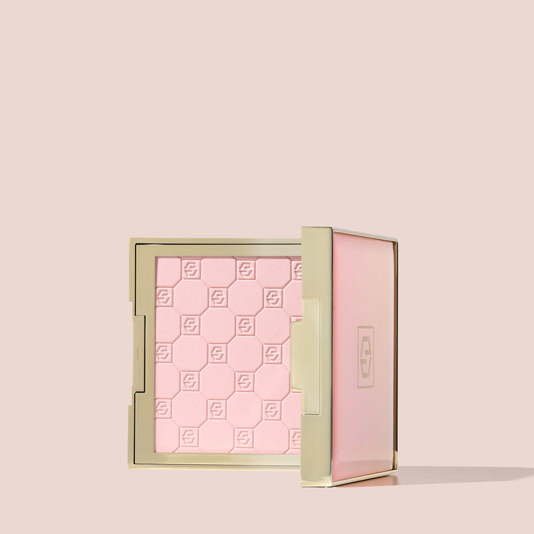 Jouer Brightening Powder open compact in pink with embossed logo pattern on a beige background.