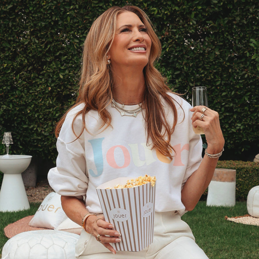 Woman wearing white Jouer pastel sweatshirt while eating popcorn outdoors on grass
