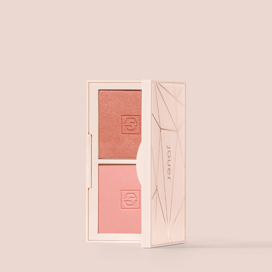 A compact makeup case with a geometric design, opened to reveal two shades of blush: a darker, shimmery pink on the top and a lighter, matte pink on the bottom for a natural flush. The brand name "Jouer Cosmetics" is printed on the inside of the lid. This product is known as the Mini Blush Bouquet.