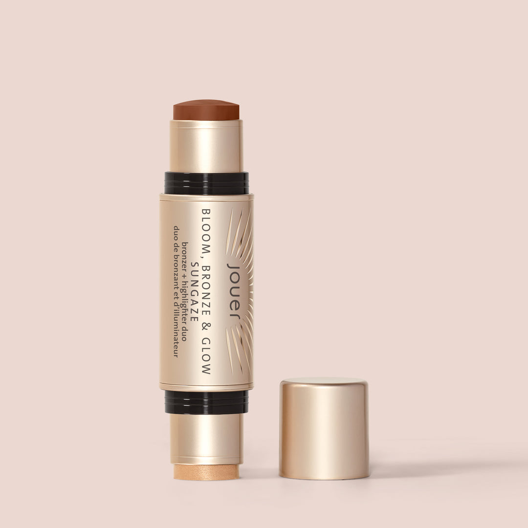 Sungaze, This dual-ended beauty stick from Jouer Cosmetics, named "Bloom, Bronze & Glow," features a bronze shade on one end and a glow highlighter on the other. It is vegan and comes with a gold cap, resting elegantly on a light surface.