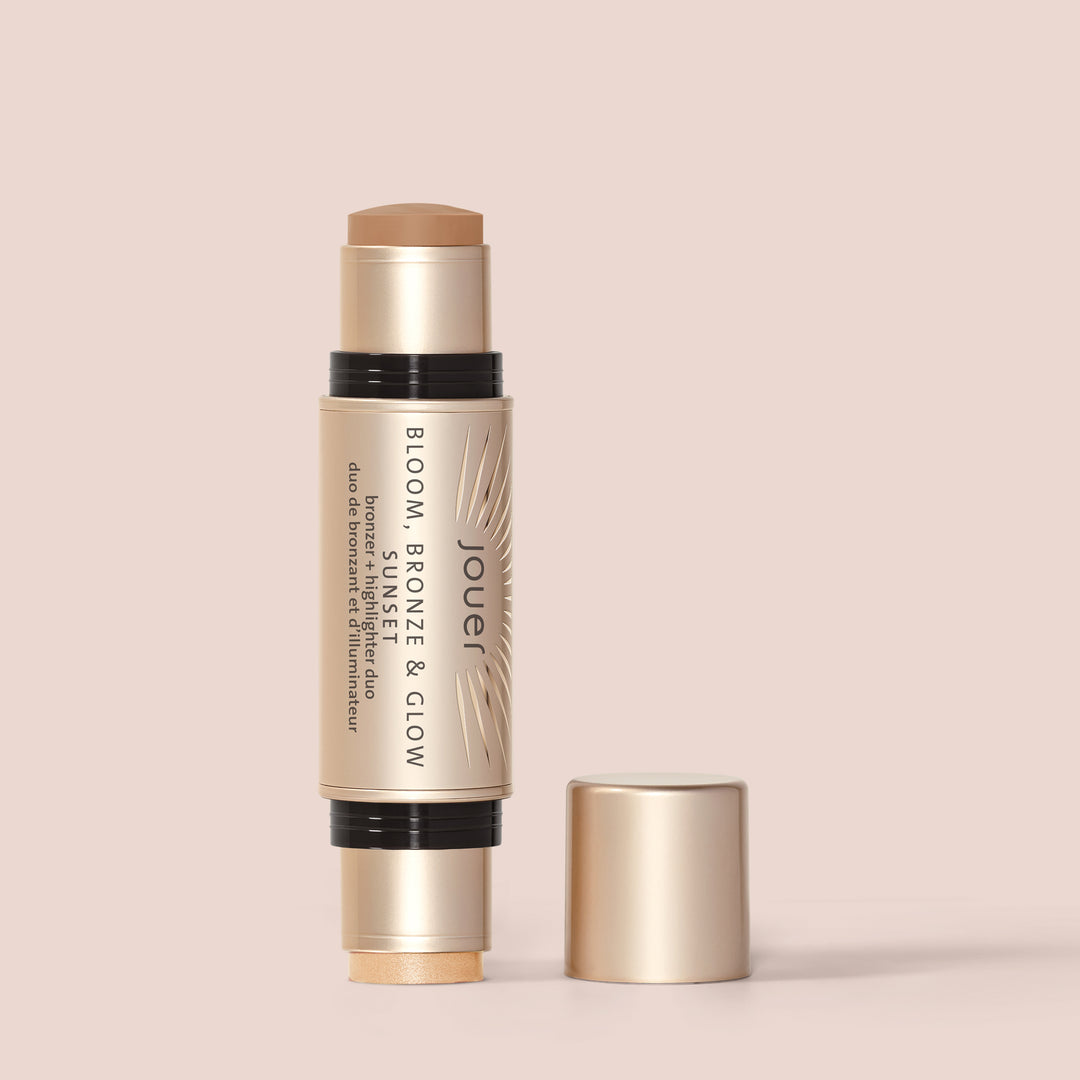 Sunset, A dual-ended cream stick labeled "Bloom, Bronze & Glow" from Jouer Cosmetics is shown open, with the cap removed from the highlighter side. This vegan stick includes a bronzer on one end and a highlighter on the other, all set against a light beige background.