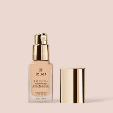  A bottle of Jouer Cosmetics Essential Crème Foundation with a gold pump and cap rests against a light beige background. The label indicates it contains 20ml (0.68 fl. oz.) and features hyaluronic acid, providing a matte, oil-free finish. It's cruelty-free and paraben-free for gentle beauty care.
