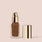 pecan, full size alt: A frosted glass bottle of Jouer Cosmetics' Essential Crème Foundation, featuring a gold pump dispenser, stands with its matching gold cap to the right. The label highlights that the foundation is cruelty-free, contains hyaluronic acid, and offers a matte and oil-free finish.