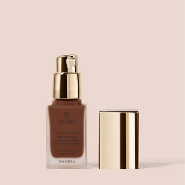 A bottle of Jouer Cosmetics Essential Crème Foundation stands with its gold cap removed and placed next to it. The 20 ml (0.68 fl oz) foundation bottle features a sleek gold pump dispenser, set against a beige background. This paraben-free, gluten-free, and cruelty-free formula ensures flawless coverage and peace of mind.