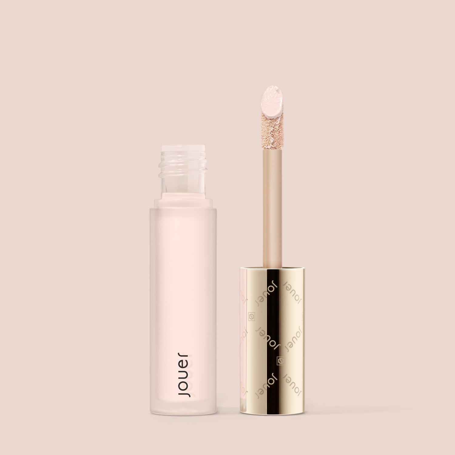 snow, A cylindrical tube of Essential Liquid Concealer from Jouer Cosmetics in a light pink hue, featuring a gold cap. The cap is removed to reveal a wand applicator with a doe-foot tip. The packaging and background are in soft beige tones, highlighting its paraben-free, vegan formula.