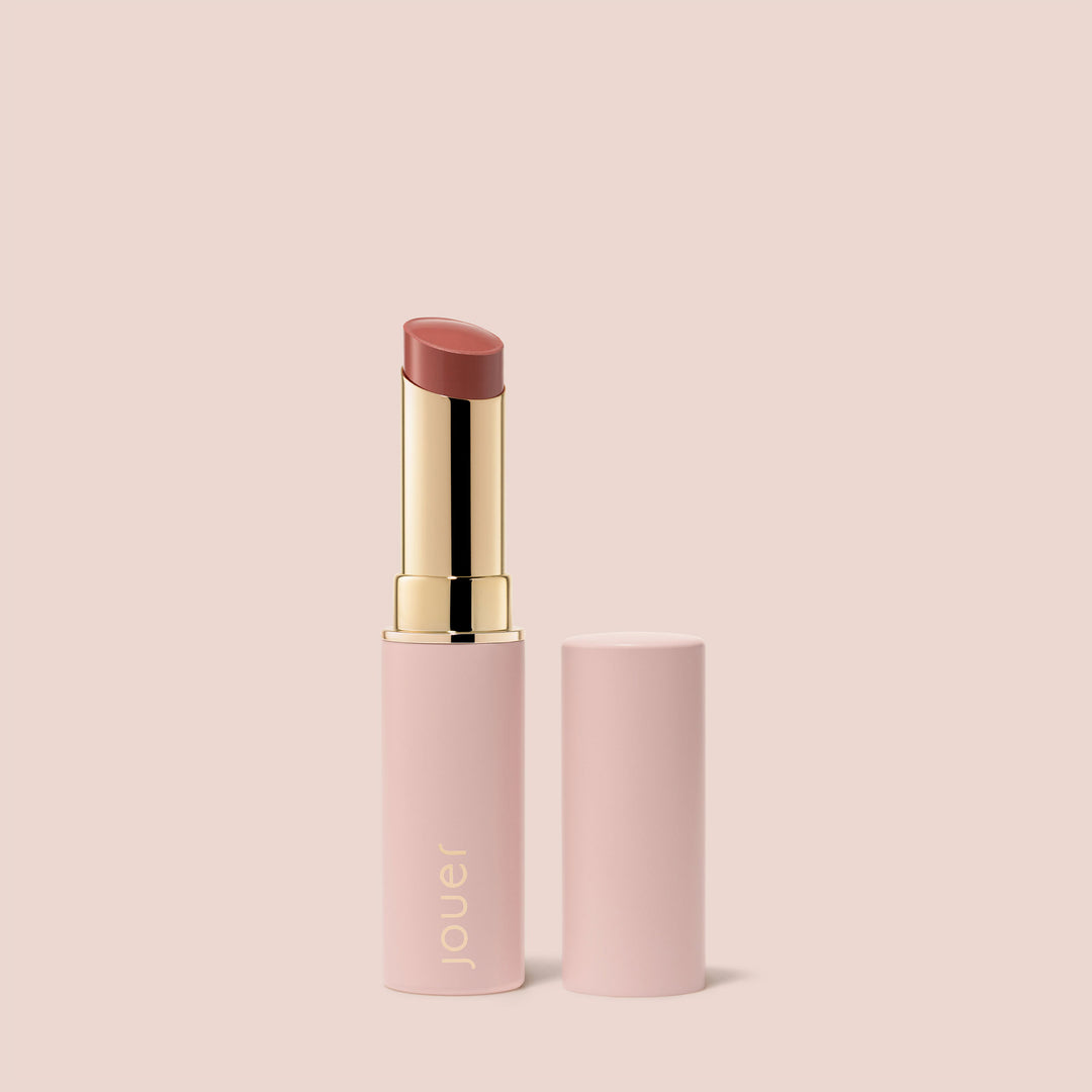 Jouer Balm Bouche pink lip balm with gold accent and matching cap against soft pink background
