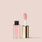 full size alt: A tube of Jouer Cosmetics' Essential Lip Oil, which is vegan and paraben-free, with its golden rectangular cap removed and placed upright beside it. The product's applicator, attached to the cap, features a pink-tinted sponge tip and stands against a light beige background.