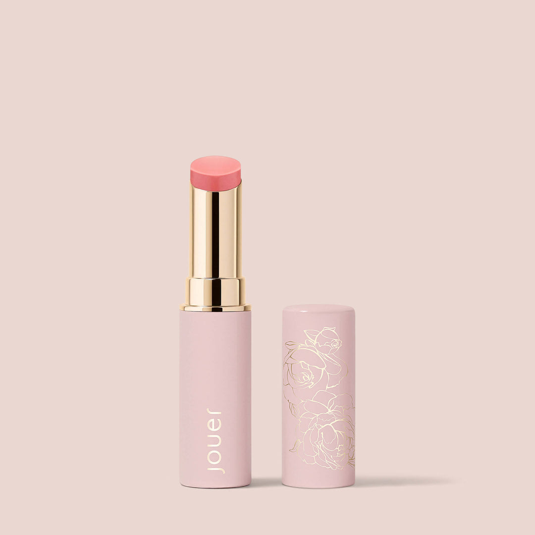 Peony, The Essential Shine Balm from Jouer Cosmetics comes in a sleek tube of gold and pastel pink, adorned with elegant floral designs. The brand name "Jouer" is printed in gold on the tube. This vegan, cruelty-free, and paraben-free balm stands upright with its cap removed, showcasing the soft pink shade against a light beige background.